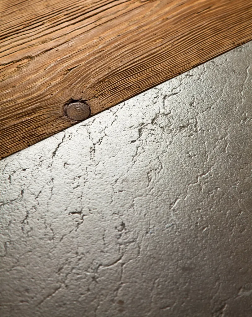 Superficie di pietra grigia chiara dalla trama irregolare accostata a una trave di legno antico con un chiodo.