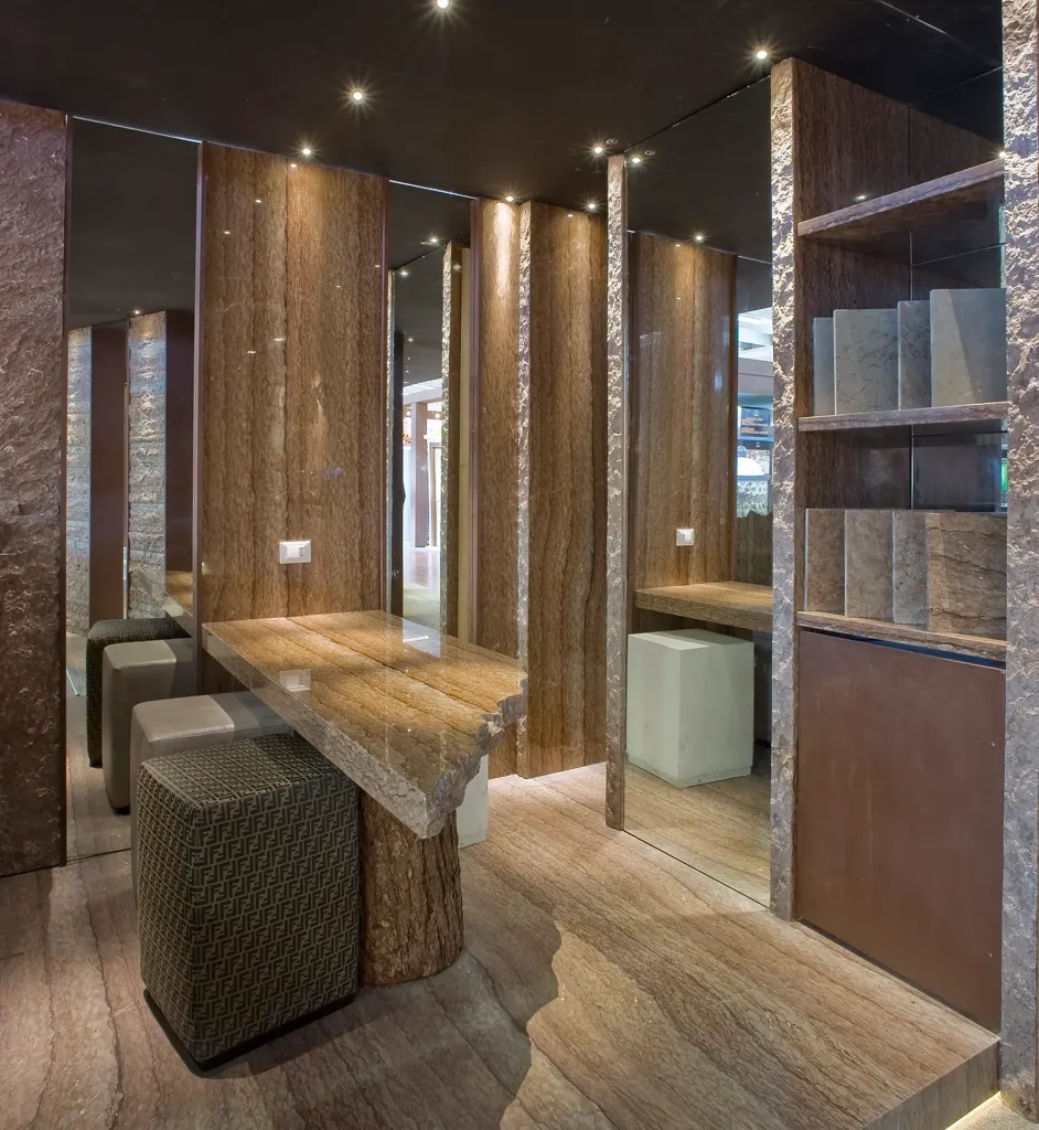 Sala con tavolo in pietra venata, sgabelli imbottiti e pareti in legno e pietra con nicchie a specchio illuminate.